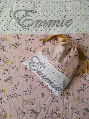 couverture et pochon assortis et personnalisés avec le prénom Emmie, on retrouve un tissu rose motif renards et oiseaux dans des branches et un tissu blanc à pois rose, ocre et gris, le prénom est en tissu gris cousu, une création 2 pommes et un mammouth