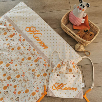 ensemble assorti couverture bébé et sac à dos pochon, mélange de couleurs blanc orange et taupe, tissu à motif pois dorés et animaux de la forêt, personnalisée avec le prénom Manon, une création 2 Pommes et un mammouth