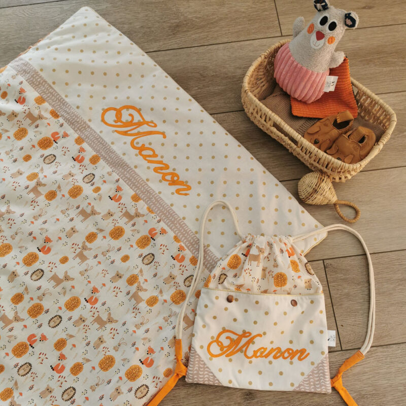 ensemble assorti couverture bébé et sac à dos pochon, mélange de couleurs blanc orange et taupe, tissu à motif pois dorés et animaux de la forêt, personnalisée avec le prénom Manon, une création 2 Pommes et un mammouth