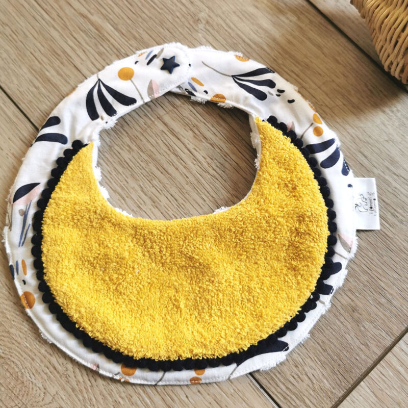 bavoir rond anti-bave pour bébé, bavoir bi-matière en éponge de coton jaune et en tissu coton blanc motif fleuri bleu marine, une petite dentelle vient réhaussée l'ensemble, une création 2 pommes et un mammouth