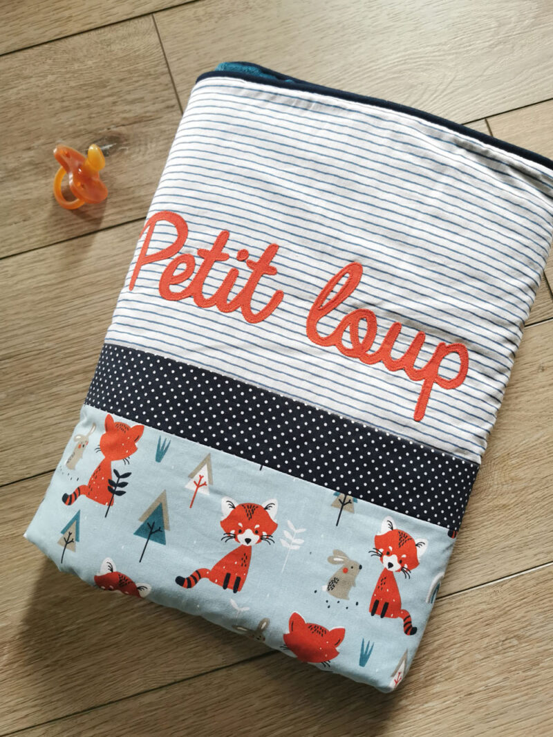 couverture pour bébé garçonprésenté roulée et présonnalisée au surprénom petit loup, tons bleus et motif avec renards une création 2 pommes et un mammouth