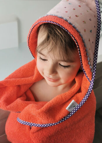 cape de bain pour enfant fabriqué en france de manière artisanale, petite fille de 3 ans emmitouflée dans une grande cape de bain rouge et violette, une création 2 pommes et un mammouth