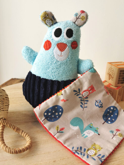 doudou pour bébé fabrication artisanale, made in france, un petit ours tout doux et coloré, bleu turquoise et rouge avec des tissus motifs animaux de la forêt, tissu oeko tex, différentes matières pour développer le sens du toucher de bébé, une création 2 pommes et un mammouth