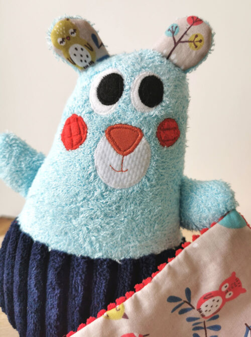 doudou pour bébé fabrication artisanale, made in france, un petit ours tout doux et coloré, bleu turquoise et rouge avec des tissus motifs animaux de la forêt, tissu oeko tex, différentes matières pour développer le sens du toucher de bébé, une création 2 pommes et un mammouth